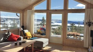 Ein gemütliches Zimmer mit Holzwänden und großen Fenstern, das einen reizvollen Blick auf eine verschneite Landschaft bietet.