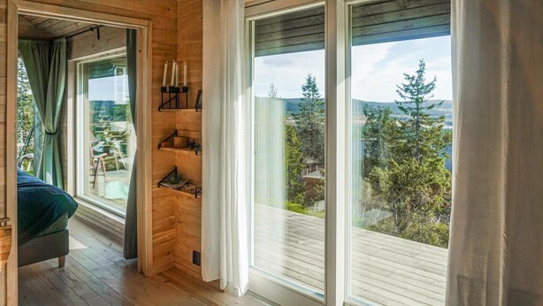 Ein gemütliches Zimmer mit Holzwänden, einem großen Fenster und Blick auf Bäume und Hügel.
