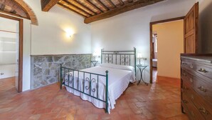 A bedroom with a stone wall, a bed with a metal frame, a dresser, and a ceiling with exposed beams. - Nice apartment in Montecatini V.C. (FI) (Montecatini V.C. (FI))