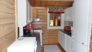 A compact kitchen with wooden walls, white cabinets, a small window with a floral curtain, and a sink. - Amazing home in Vikersund with sauna (Vikersund)