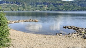 A calm lake with a rocky shoreline and a forested hill in the background. - Amazing home in Vikersund with sauna (Vikersund)