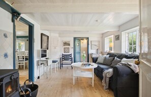 A cozy living room with a fireplace, a sofa, a dining table, and a blue door. - 3 bedroom cozy home in Fanø (Fanø)