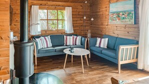 Acogedor interior de cabaña con paredes de madera, un conjunto de sofás, una mesa y una chimenea.