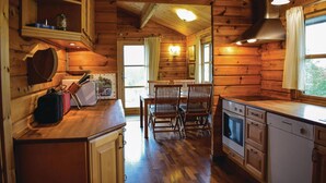 Interior de una cabaña de madera con comedor, cocina y un amplio ventanal.