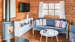 Interior acogedor de una cabaña con chimenea, sofá y televisor montado en la pared.