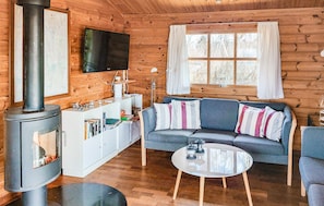 Ein gemütliches Blockhaus-Interieur mit Kamin, einer Couch und einem an der Wand befestigten Fernseher.