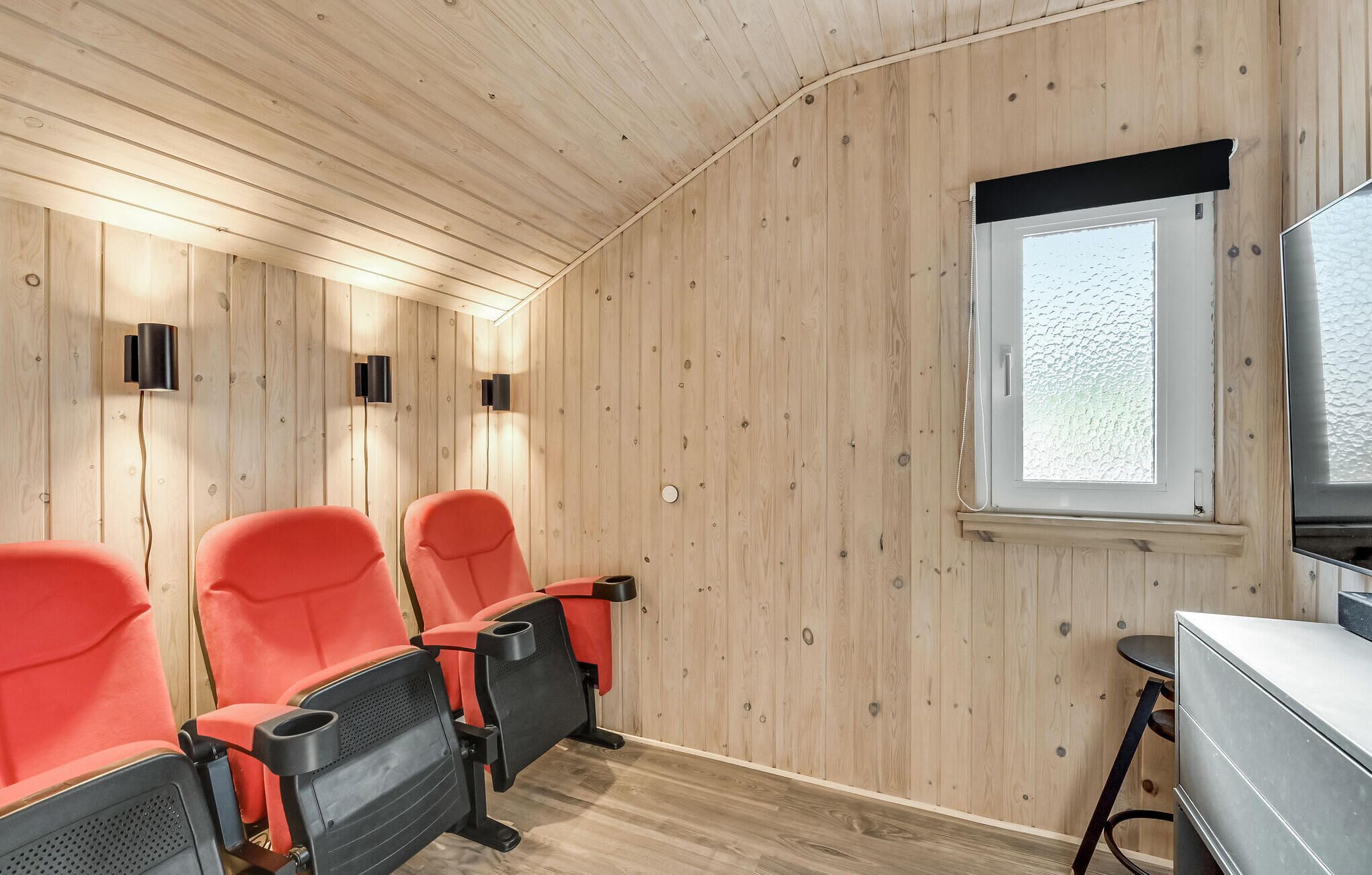 A room with wooden walls and ceiling, two red chairs with black armrests, a small table, and a window with frosted glass.