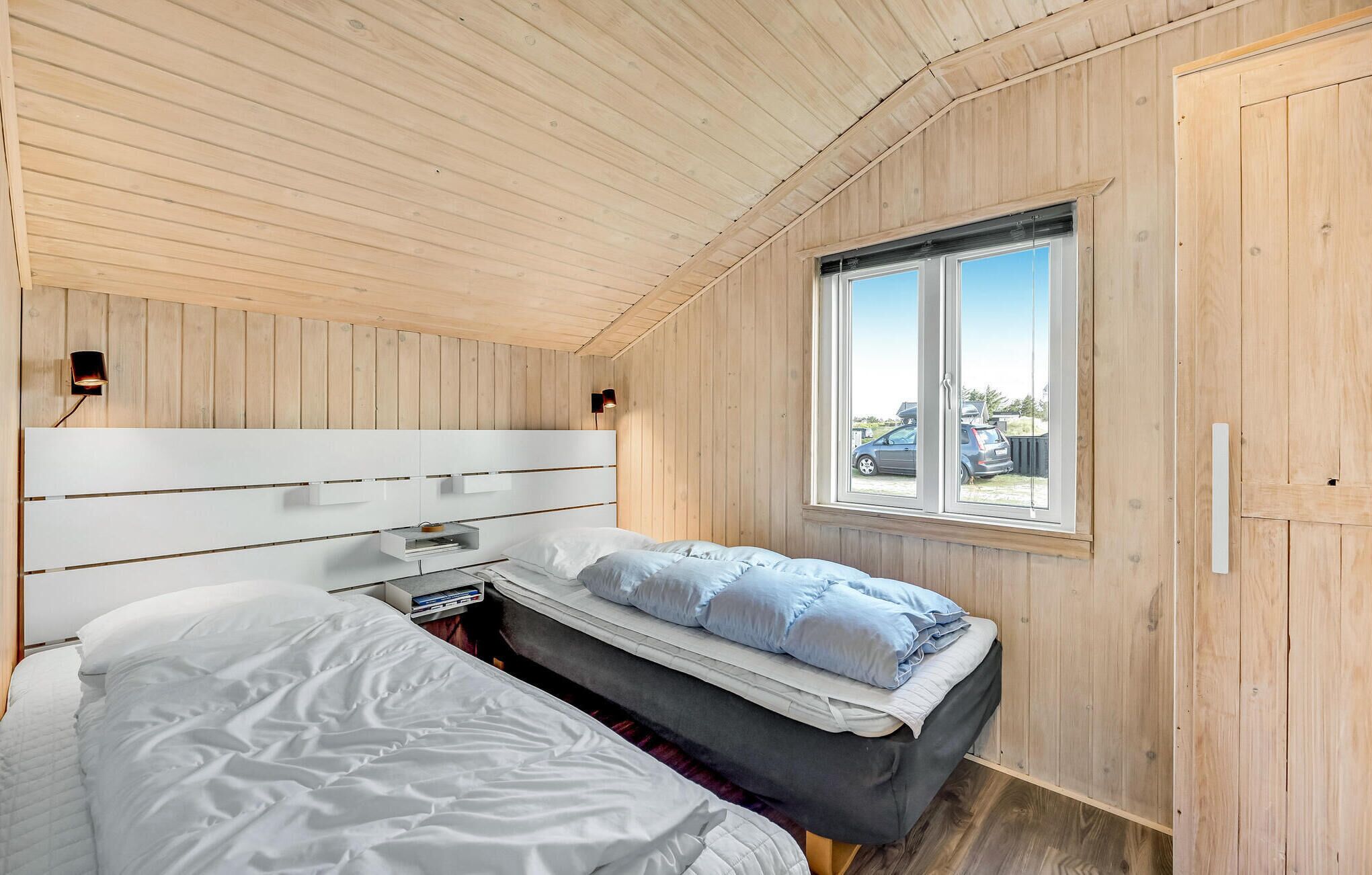 A bedroom with a bunk bed, a bedside table, a lamp, and a window with a view of the outside.