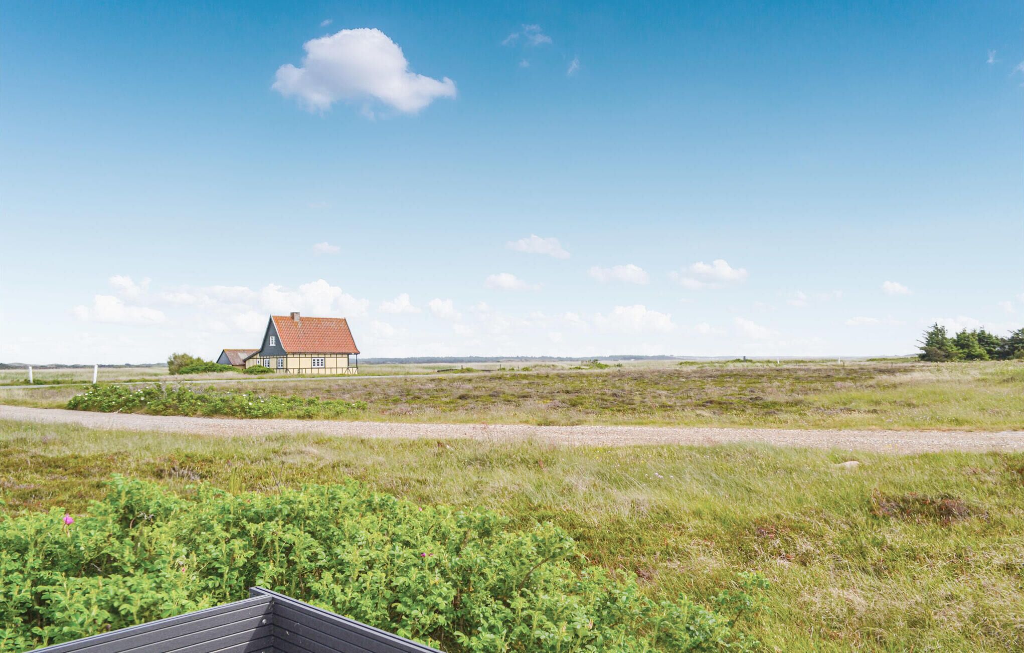 Une maison de campagne avec un toit rouge et des murs blancs, entourée de champs ouverts et sous un ciel dégagé.