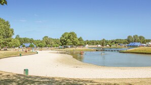 A sandy beach area with a calm water body, surrounded by trees and tents.