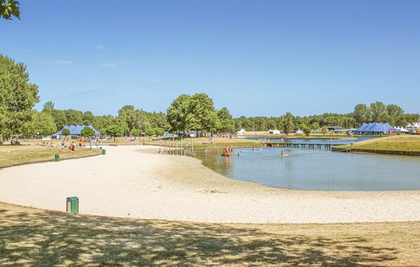A sandy beach area with a calm water body, surrounded by trees and tents.