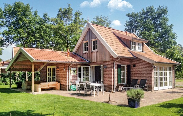 A two-story house with a brick exterior, a sloped roof, and a covered patio area with outdoor furniture.