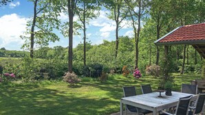 An outdoor patio with a table and chairs, surrounded by lush greenery and flowering plants.