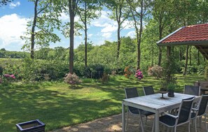 An outdoor patio with a table and chairs, surrounded by lush greenery and flowering plants.