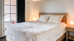 A bedroom with a wooden bed, two bedside lamps, a window with curtains, and a door.