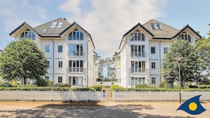 En moderne toetagers bolig med en symmetrisk facade, store vinduer og et hvidt stakkeværk foran.
