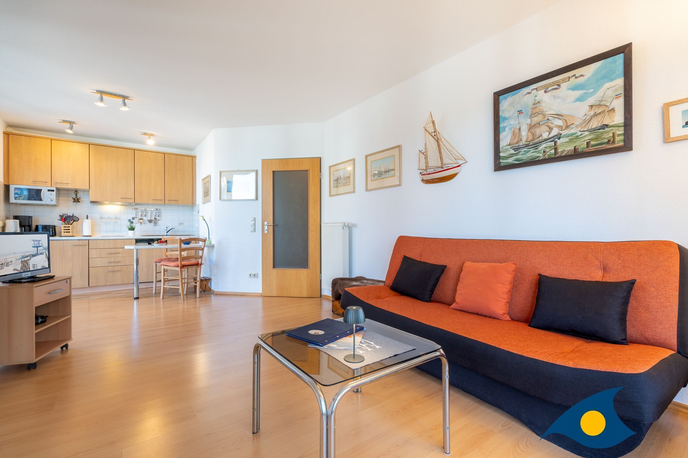 A modern living room with a sofa, a glass coffee table, a dining area with a chair, and a kitchen in the background.
