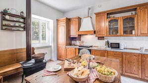 A kitchen with wooden cabinets, a stove, and a dining table set with bread, grapes, and a bottle.