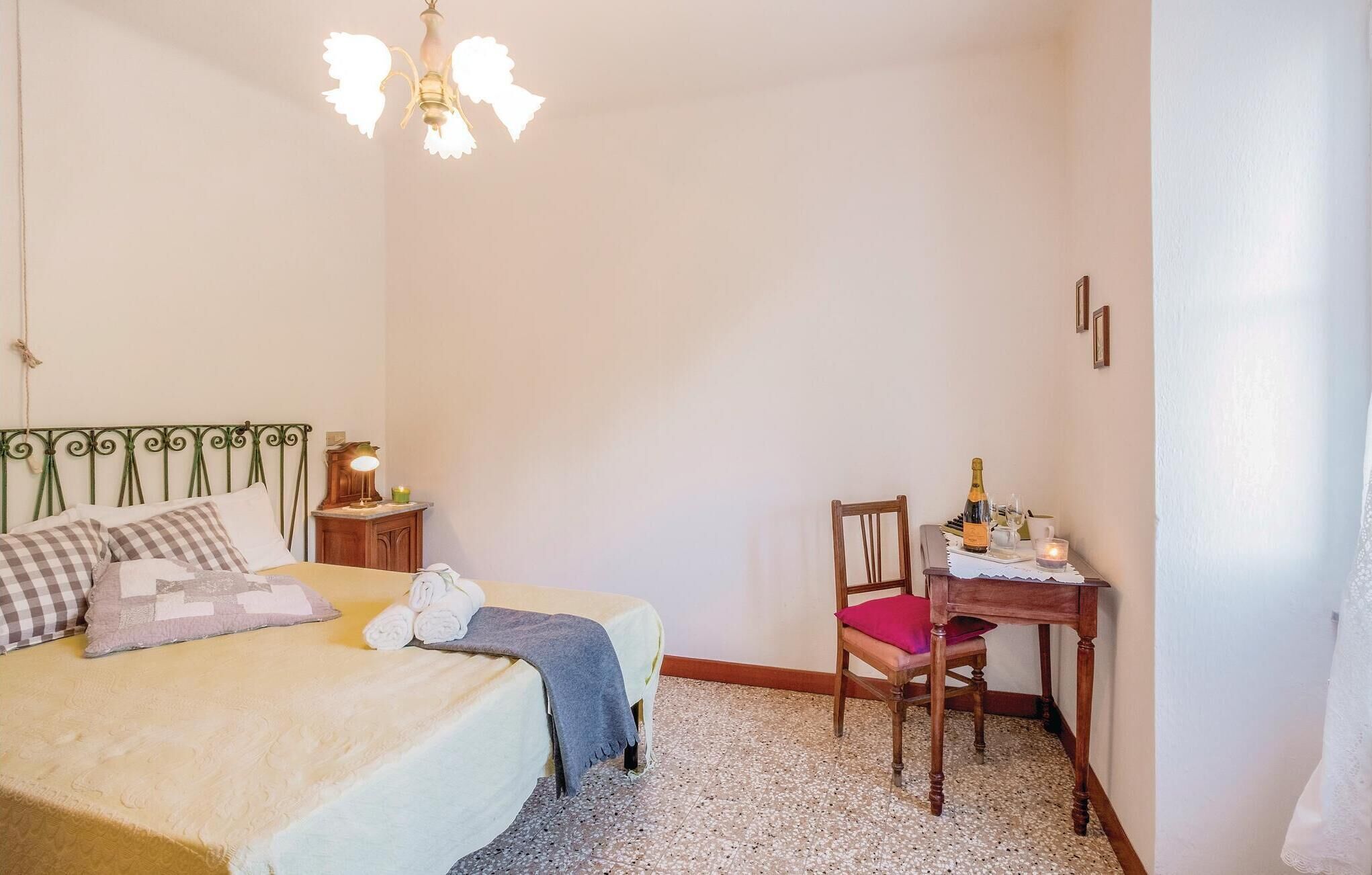 A bedroom with a bed, a desk with a chair, a lamp, and a chandelier.