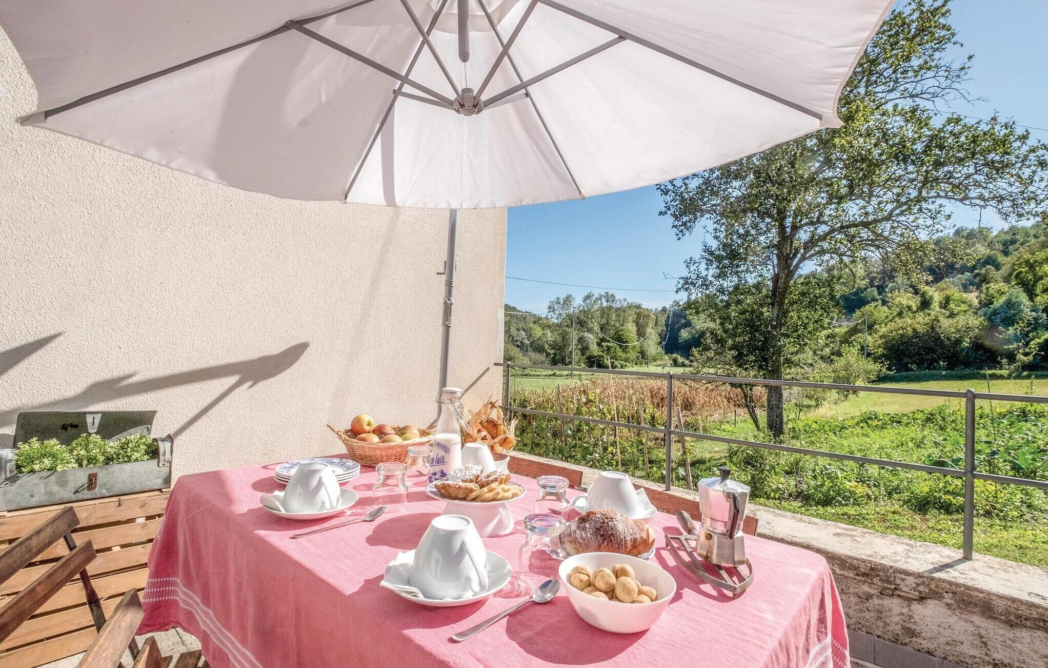 An outdoor dining area with a table set for breakfast, including bread, pastries, and a coffee machine, overlooking a scenic landscape.