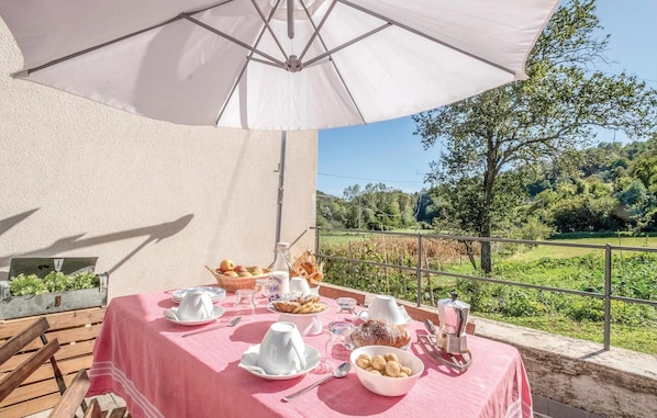 Uma área de refeições ao ar livre com uma mesa posta para o café da manhã, incluindo pão, doces e uma máquina de café, com vista para uma paisagem deslumbrante.