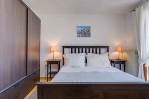 A bedroom with a large bed, two bedside tables with lamps, a wooden wardrobe, a framed picture on the wall, and a radiator.