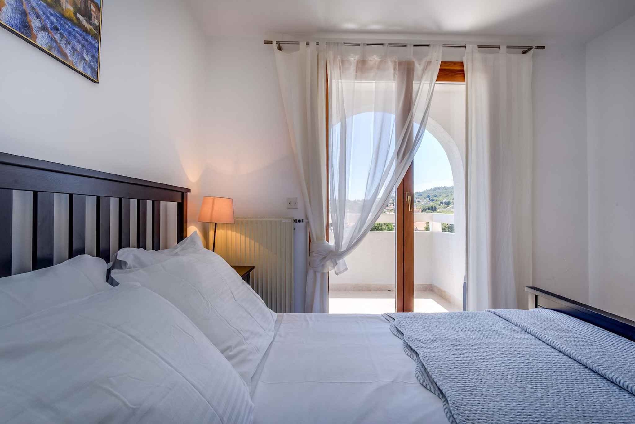 Ein Schlafzimmer mit einem großen Bett, einer Nachttischlampe und Blick auf einen Balkon.