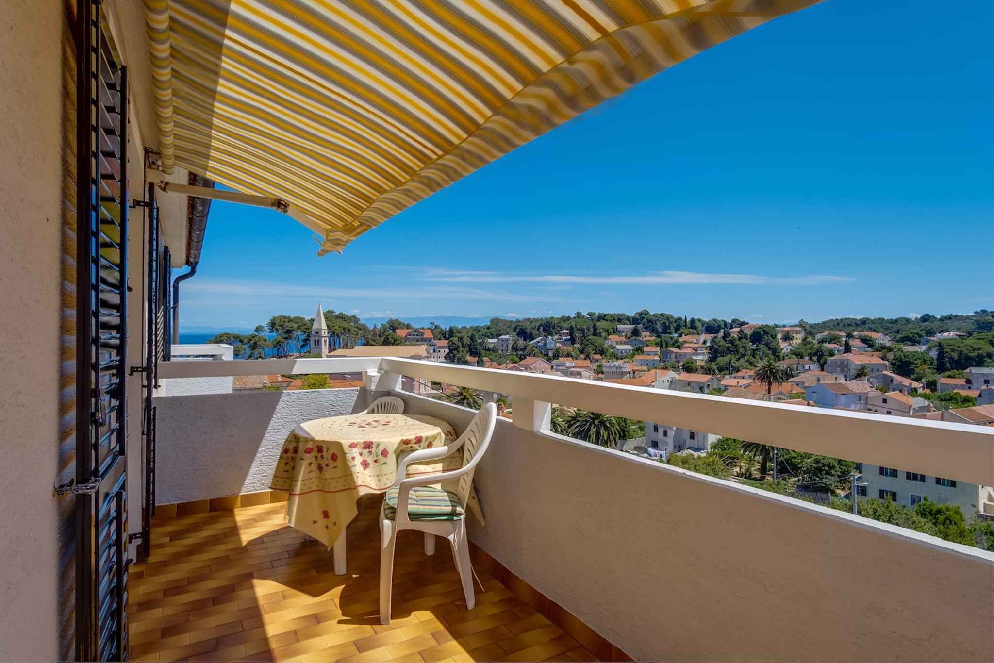 A balcony with a table and chairs, a striped awning, and a view of a town.