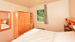 Un dormitorio con cama, armario de madera, ventana con vistas a la vegetación y espejo.