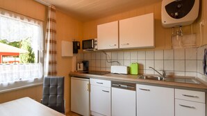 Una cocina compacta con armarios blancos, microondas, cafetera y lavavajillas.