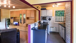 Una cocina compacta con armarios de madera, un microondas, un tostador y una pequeña zona de comedor con una silla.