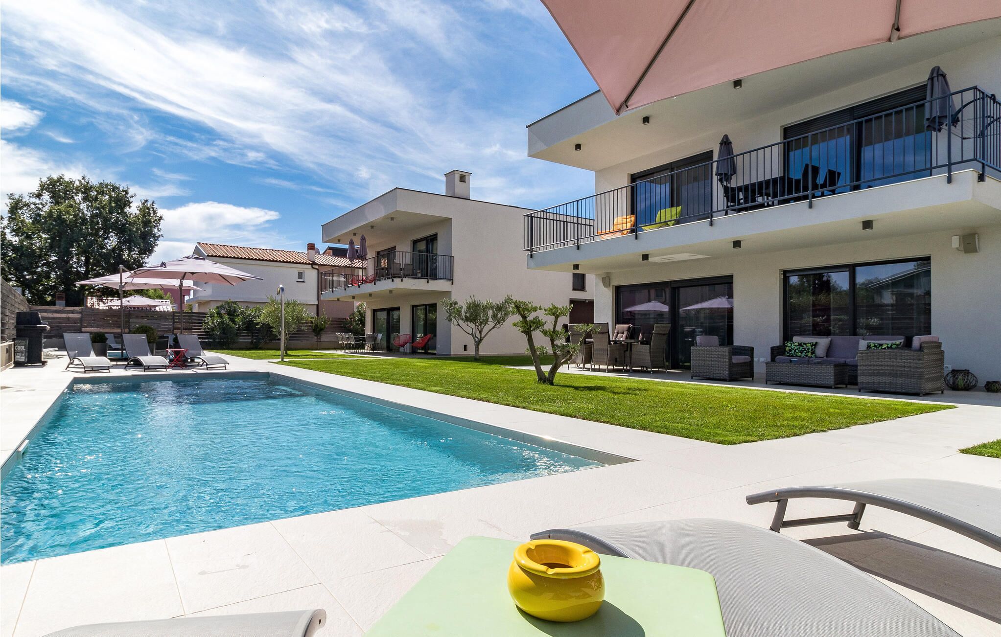 Ein modernes, zweistöckiges Haus mit Swimmingpool, Außenbereich zum Sitzen und einem gepflegten Rasen.