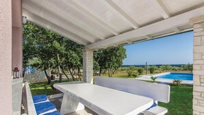An outdoor patio with a white table and blue cushioned seating, overlooking a swimming pool and lush greenery. - Lovely home in Cubani (Cubani)