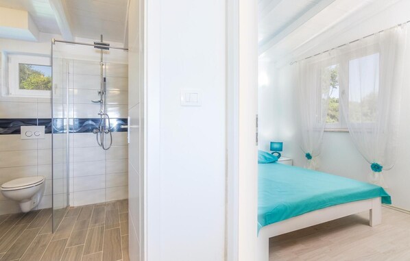 A modern bathroom with a shower, toilet, and a bed with a blue bedspread.