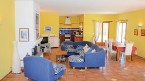 Una sala de estar con sofás azules, una zona de comedor con mantel rojo y una cocina con salpicadero de azulejos azules.