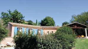Un edificio con techo de tejas, un pequeño porche y una zona de piscina con sillas de descanso.