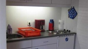 Cocina compacta con armarios blancos, un lavamanos y una estufa. Hay una cesta roja en la encimera y una olla azul colgada en la pared.