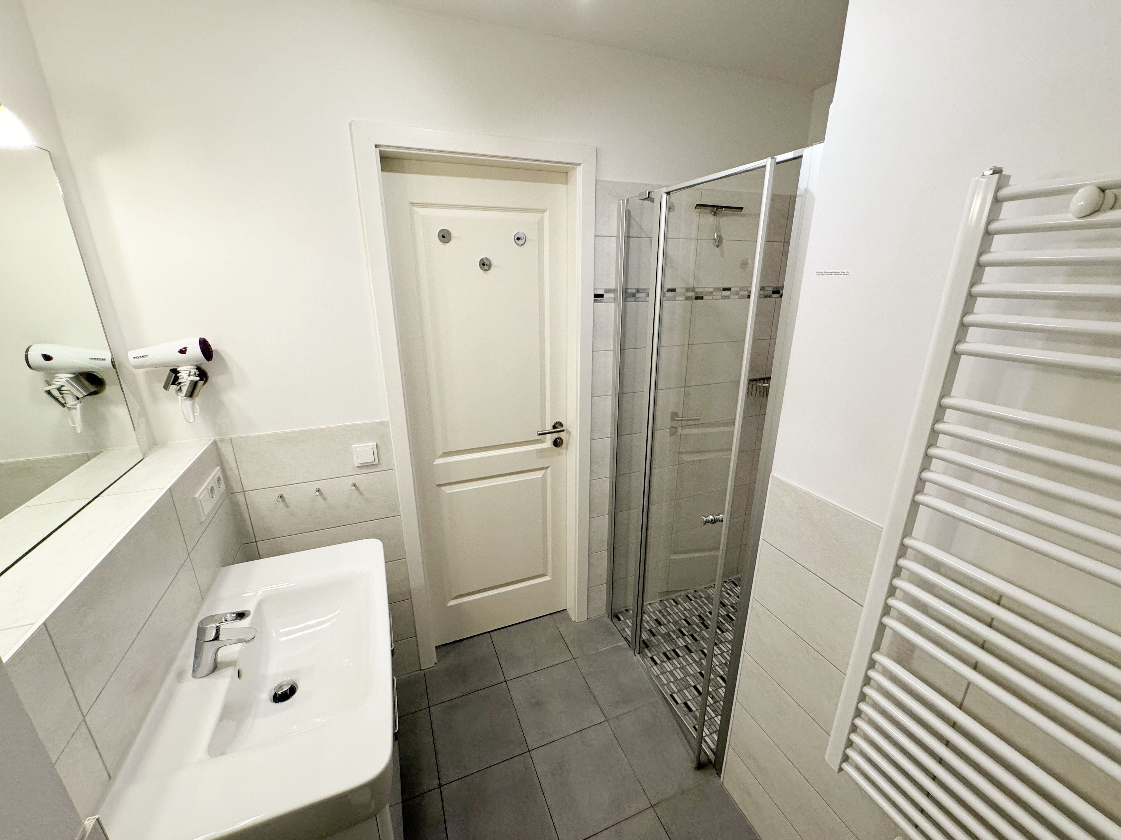 Un baño con lavabo, espejo, puerta y zona de ducha.