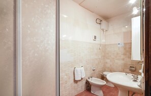 Bathroom features a glass shower enclosure, pedestal sink, and bidet, with beige tile walls and a towel rack.
