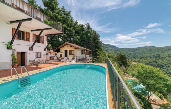 Relax by the serene pool surrounded by lush greenery and rolling hills, with a comfortable seating area nearby.