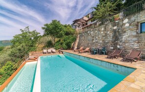 Relax by the serene pool surrounded by lush greenery and a stone wall, with lounge chairs and a table for unwinding.