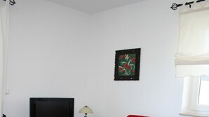 A living room with a red sofa, a black entertainment unit, a television, and a table with a white tablecloth. - Apartment Wiesenblick 1-1 bedroom up to max. 2 pers. - Vacation home Wiesenblick (Karlshagen)