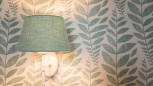 A wall-mounted lamp with a textured shade against a leaf-patterned wallpaper. - Superior Double Room - Bio Design Boutique Hotel Landhaus St. Georg (Bad Wiessee)