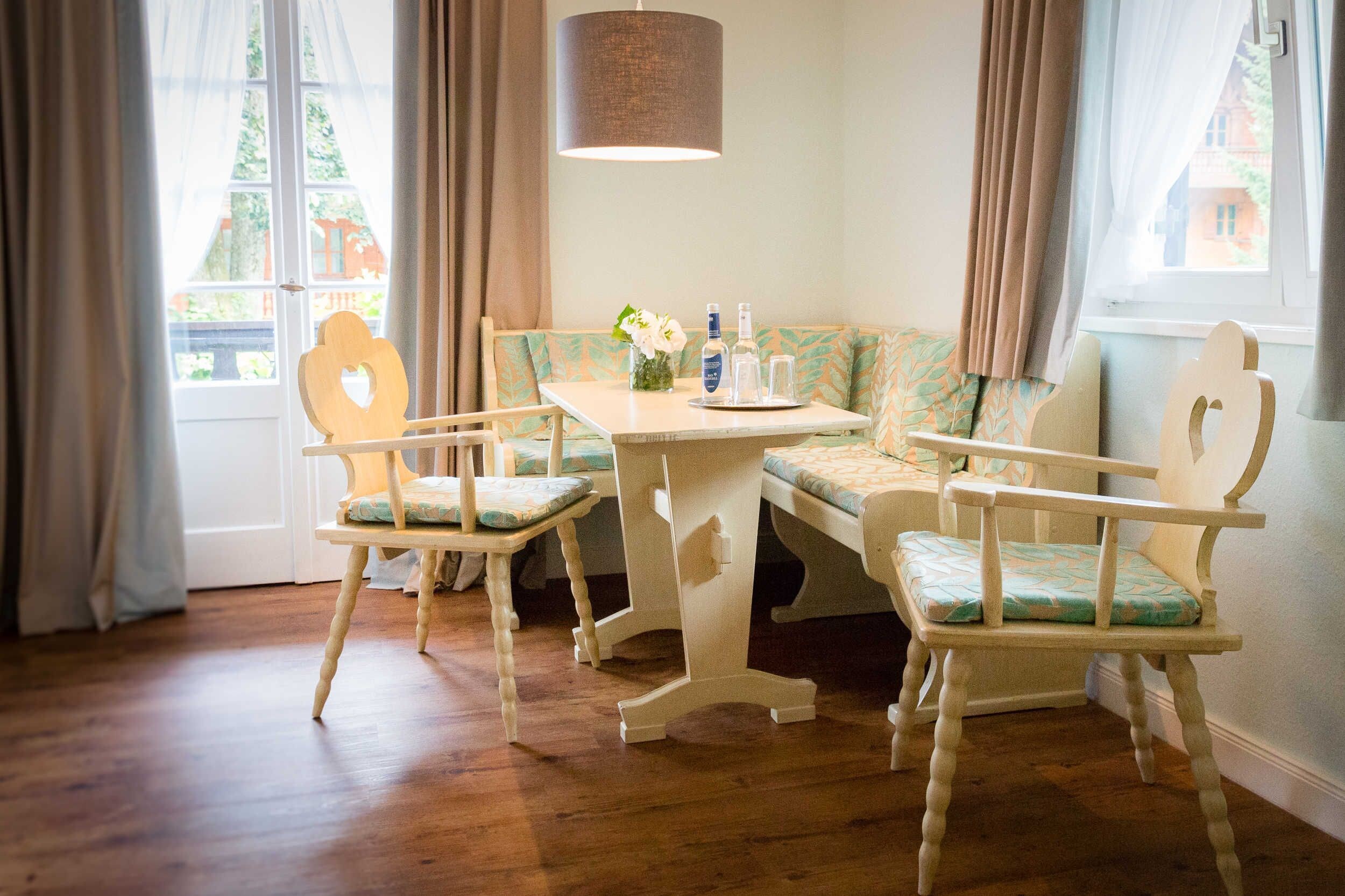 Ein Zimmer mit Holzboden, einem Tisch mit Stühlen, einer Bank und einer Pendelleuchte.
