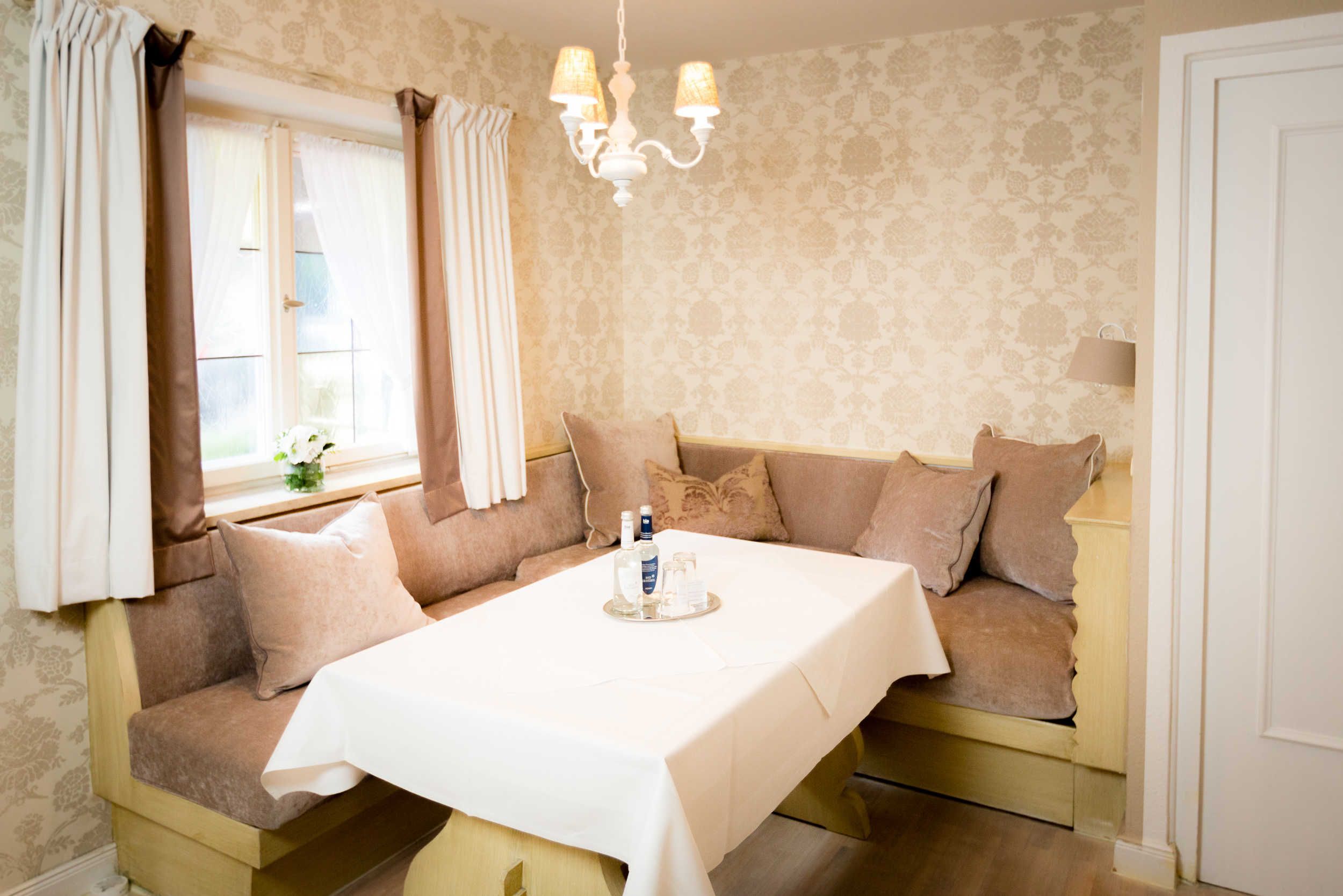 A room with a sofa bed, a table with a tray of items, a chandelier, and patterned wallpaper.