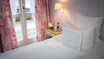 Ein Hotelzimmer mit Bett, einem Nachttisch mit Pflegeprodukten, einer Lampe und Blick ins Freie durch eine Tür.