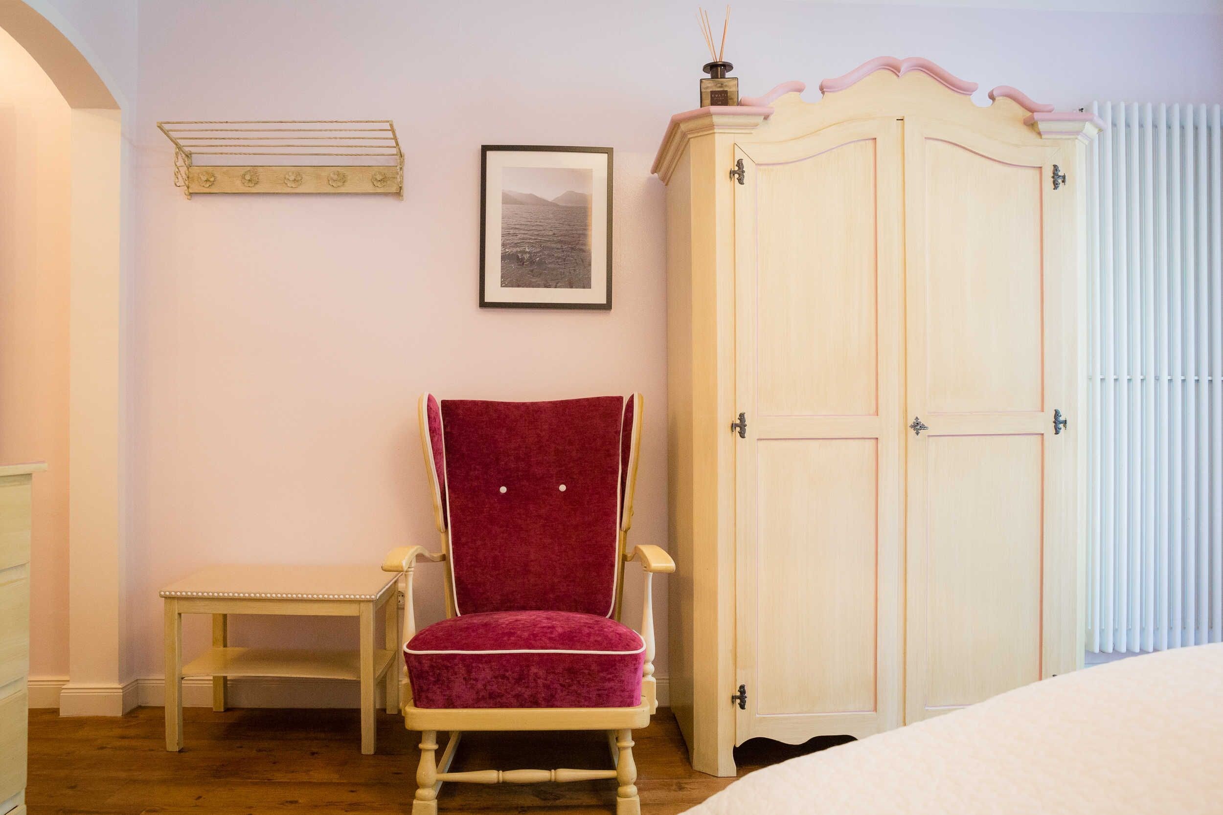 A bedroom with a wooden bed, a red chair, a white wardrobe, and a framed picture on the wall.