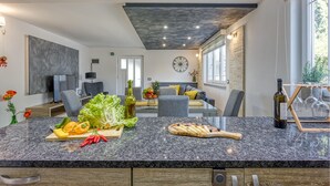 Una cocina moderna con encimera de granito, zona de comedor con sofá gris y un amplio ventanal que proporciona luz natural.
