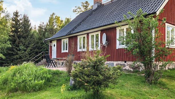 Een rode houten woning met een donker dak, witte ramen en een klein terras met stoelen.