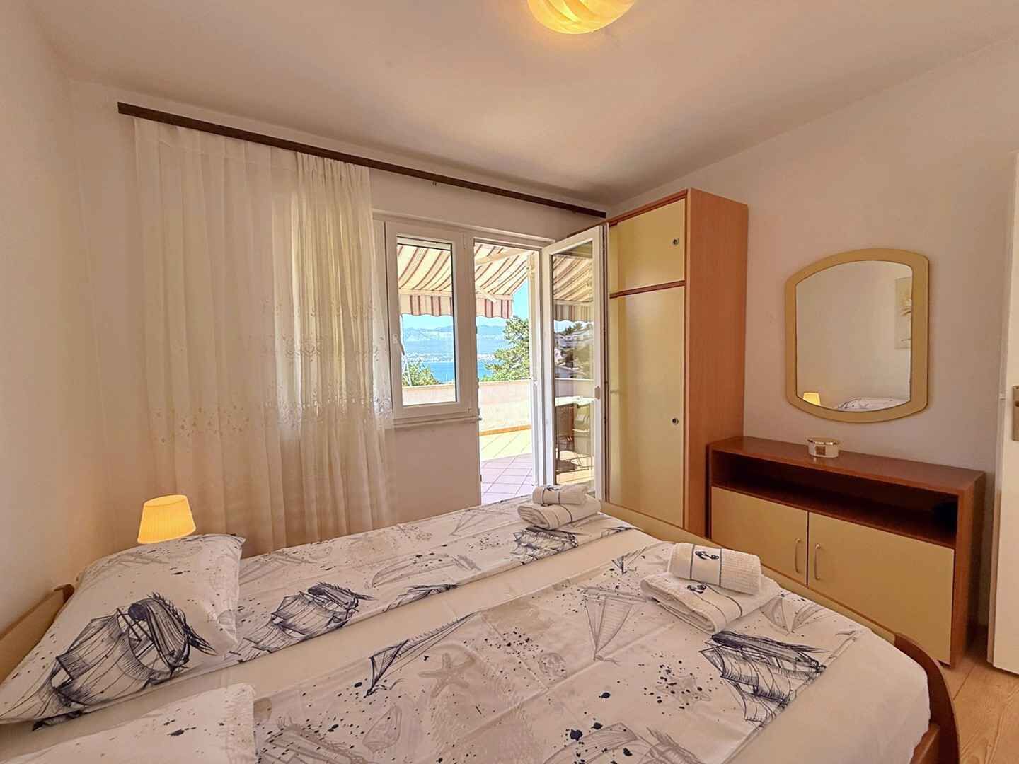 Une chambre à coucher avec un lit, une table de chevet, un miroir et une vue sur l’extérieur.